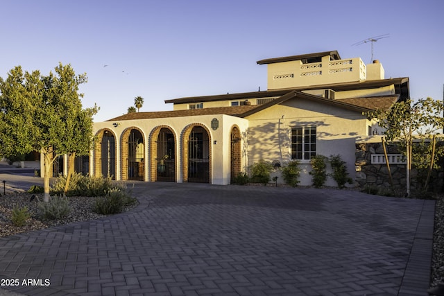 view of front of house with stucco siding, decorative driveway, and a chimney
