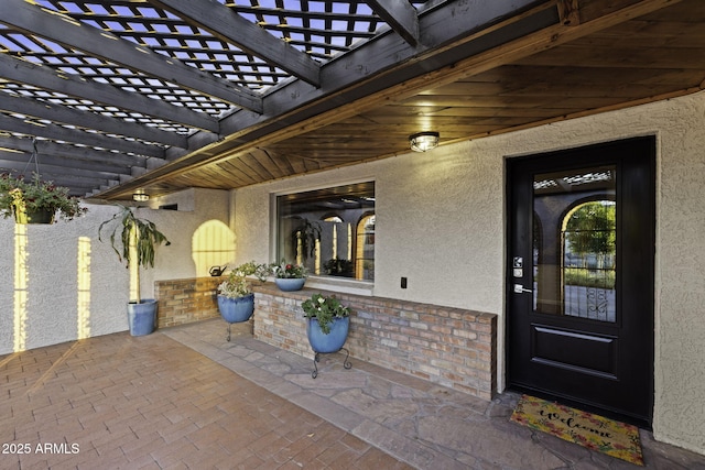 entrance to property featuring stucco siding and a pergola