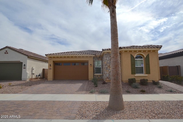 mediterranean / spanish-style home with a tile roof, decorative driveway, an attached garage, and stucco siding