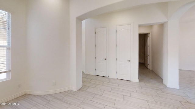 unfurnished room with arched walkways and baseboards