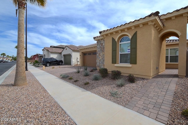 view of side of property featuring a tile roof, an attached garage, driveway, and stucco siding