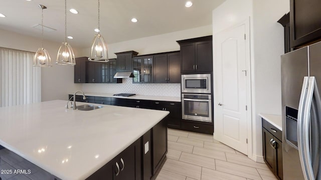 kitchen with under cabinet range hood, a sink, backsplash, appliances with stainless steel finishes, and light countertops