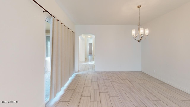 empty room with wood finish floors, baseboards, arched walkways, and a chandelier