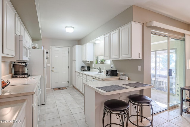 kitchen with kitchen peninsula, a breakfast bar, sink, light tile patterned floors, and white cabinetry