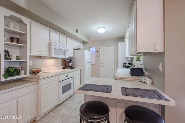 kitchen featuring light tile patterned floors, kitchen peninsula, white appliances, a breakfast bar, and white cabinets