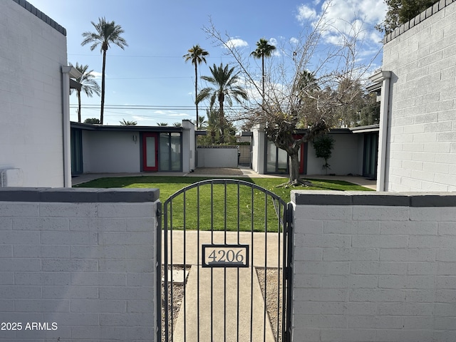 view of gate featuring a fenced front yard and a lawn