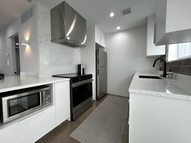 kitchen with visible vents, appliances with stainless steel finishes, a sink, wall chimney range hood, and modern cabinets