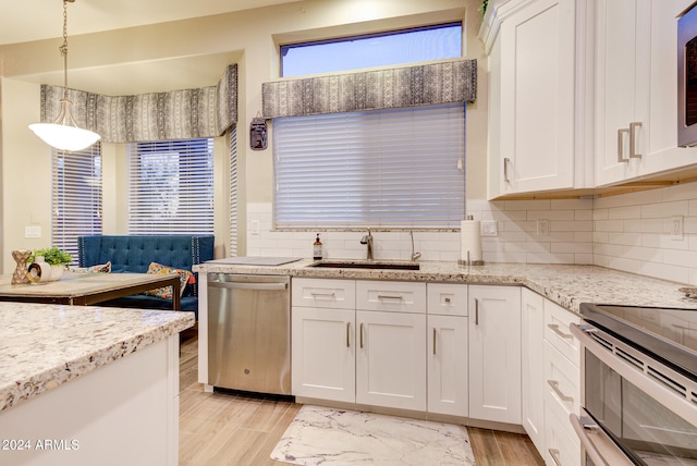 kitchen with white cabinets, hanging light fixtures, appliances with stainless steel finishes, light hardwood / wood-style floors, and sink