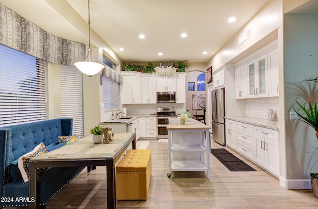 kitchen with appliances with stainless steel finishes, white cabinetry, light hardwood / wood-style floors, and backsplash