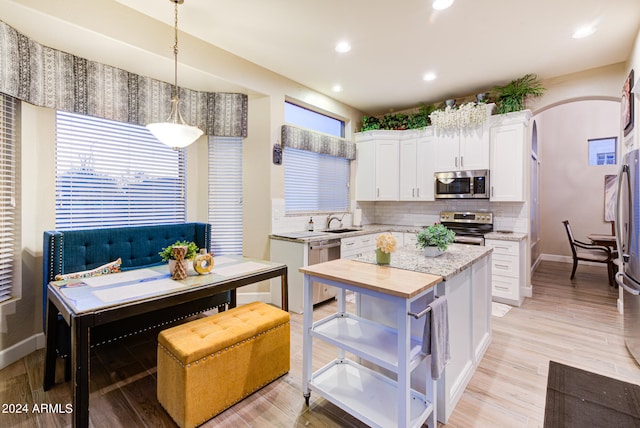 kitchen featuring appliances with stainless steel finishes, hanging light fixtures, white cabinets, and plenty of natural light