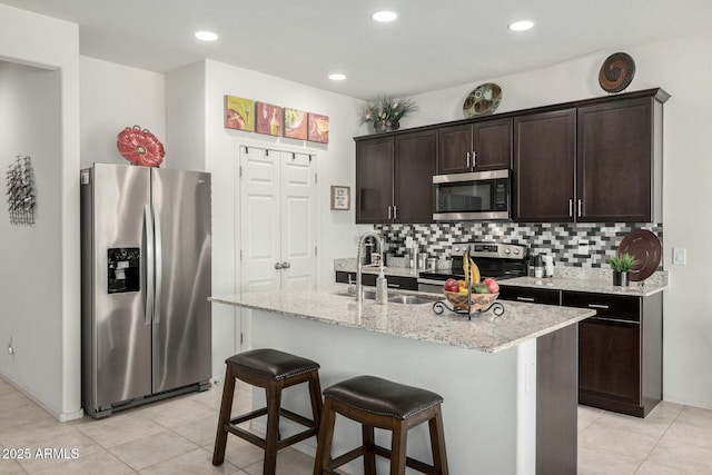 kitchen featuring sink, appliances with stainless steel finishes, backsplash, dark brown cabinetry, and a center island with sink