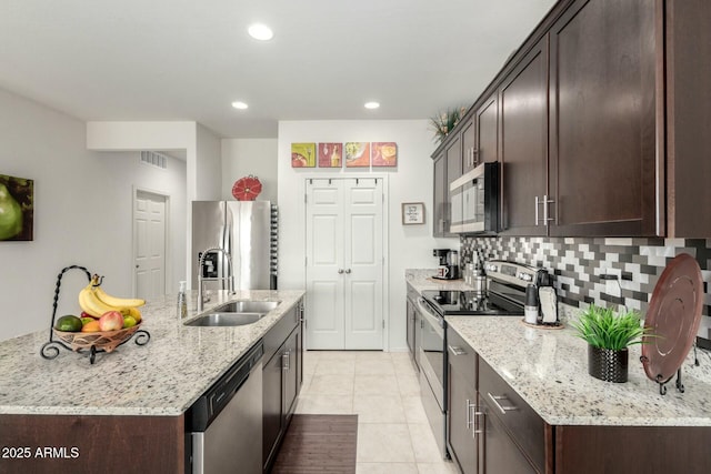 kitchen featuring sink, stainless steel appliances, light stone counters, tasteful backsplash, and a center island with sink