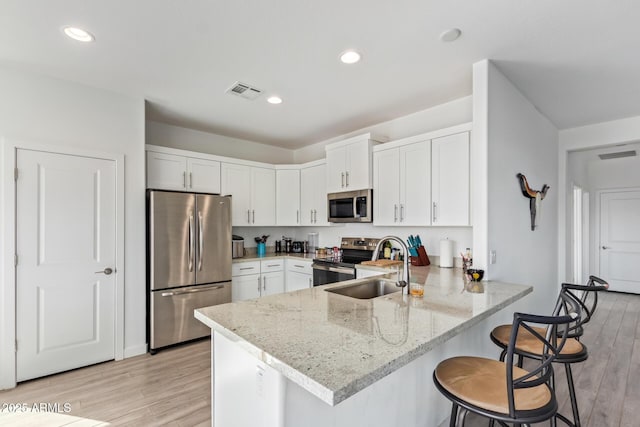 kitchen with white cabinetry, light hardwood / wood-style floors, kitchen peninsula, stainless steel appliances, and light stone countertops