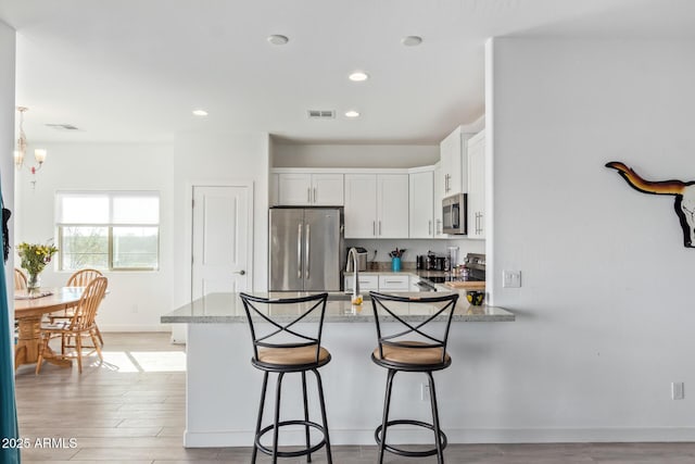 kitchen featuring a breakfast bar area, white cabinets, kitchen peninsula, stainless steel appliances, and light stone countertops