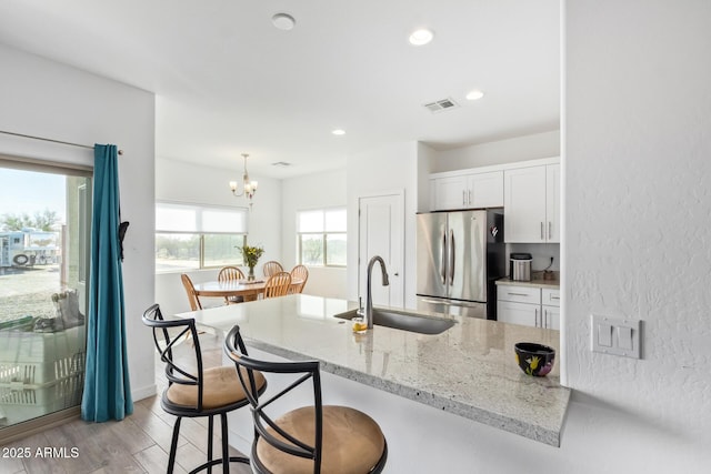 kitchen with white cabinets, hanging light fixtures, sink, and stainless steel fridge