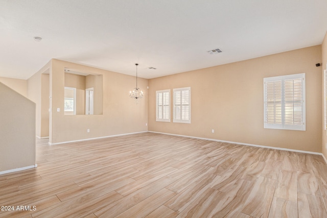 spare room featuring an inviting chandelier and light hardwood / wood-style flooring