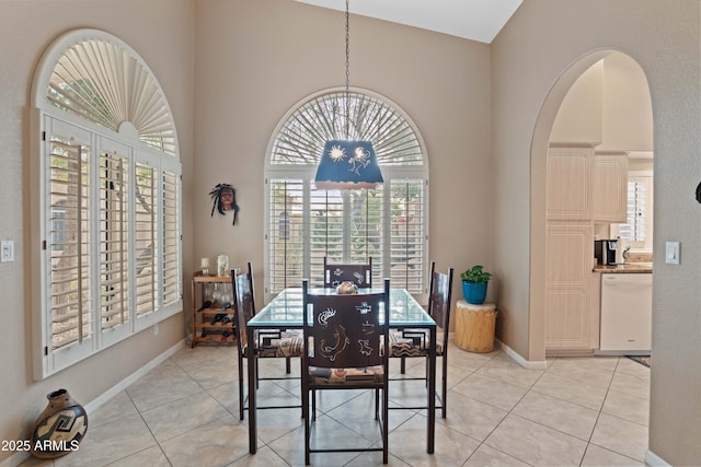 dining space featuring high vaulted ceiling, arched walkways, light tile patterned flooring, and baseboards