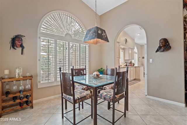 dining space featuring arched walkways, light tile patterned flooring, vaulted ceiling, and baseboards