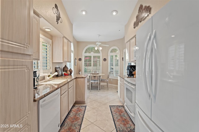 kitchen with light stone counters, light tile patterned flooring, a sink, white appliances, and baseboards