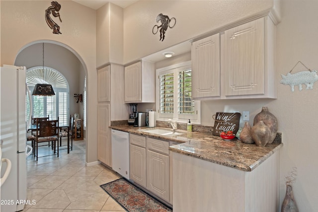 kitchen featuring arched walkways, light tile patterned floors, stone countertops, white appliances, and a sink