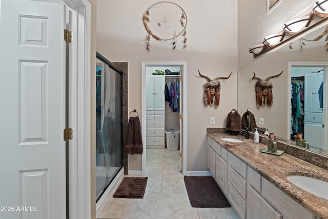 bathroom with double vanity, tile patterned flooring, a spacious closet, a shower stall, and a sink