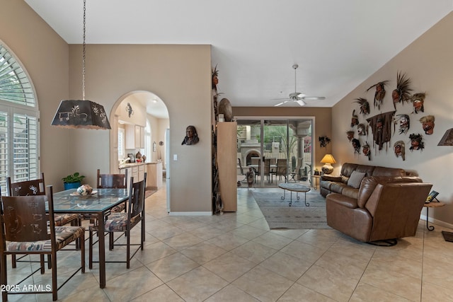 dining room with arched walkways, light tile patterned flooring, a ceiling fan, and baseboards