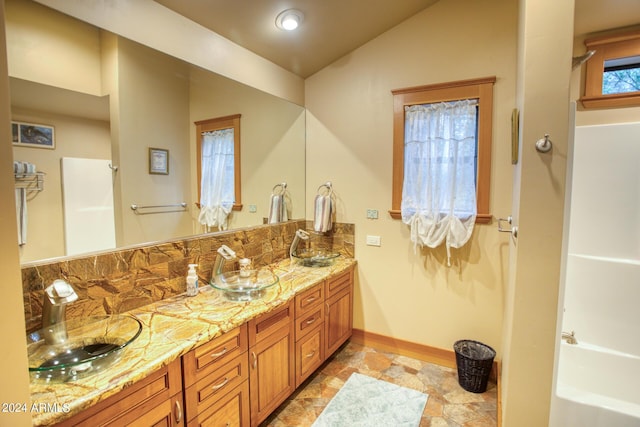 bathroom with vaulted ceiling, double vanity, a sink, and baseboards