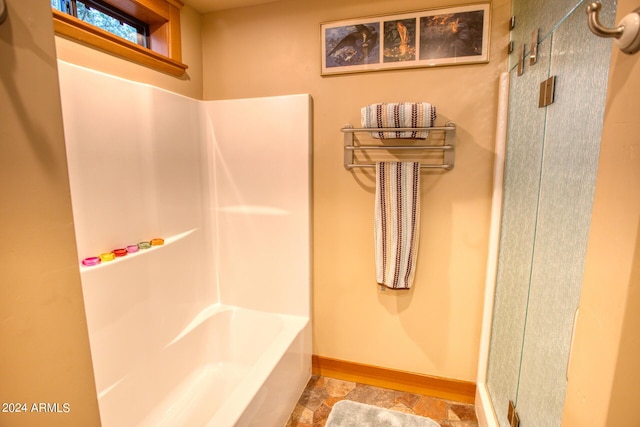 bathroom with stone finish flooring, tub / shower combination, and baseboards