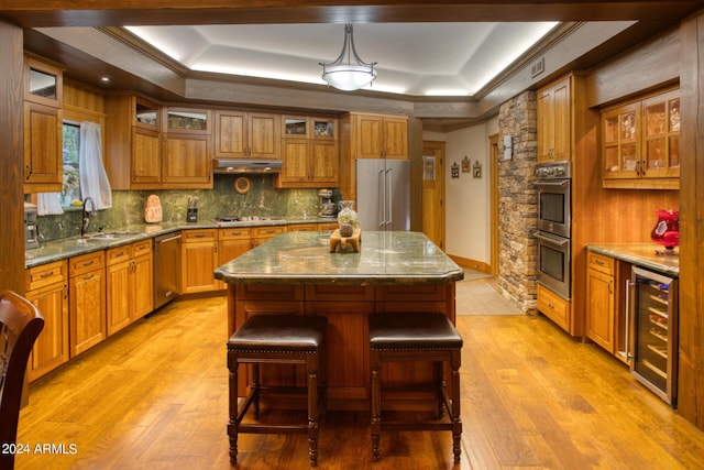 kitchen featuring beverage cooler, a tray ceiling, stainless steel appliances, under cabinet range hood, and a sink