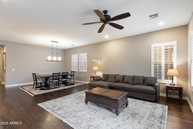 living area featuring visible vents, baseboards, dark wood-style flooring, and ceiling fan with notable chandelier