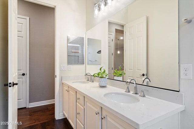 full bathroom featuring a sink, baseboards, wood finished floors, and double vanity