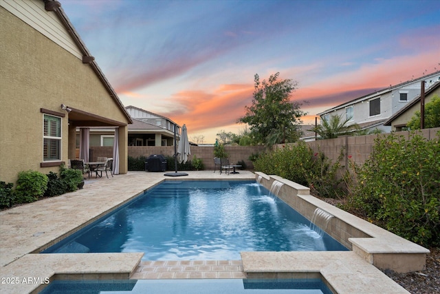 pool at dusk with a fenced backyard, a pool with connected hot tub, and a patio