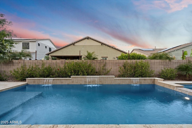 pool at dusk with a fenced backyard and a pool with connected hot tub