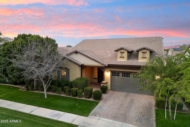 view of front facade with stucco siding, a tiled roof, decorative driveway, and a front yard