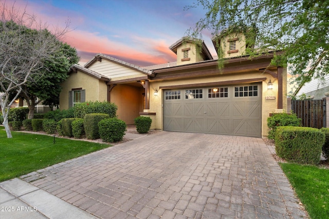 view of front of house featuring fence, stucco siding, a garage, a tiled roof, and decorative driveway