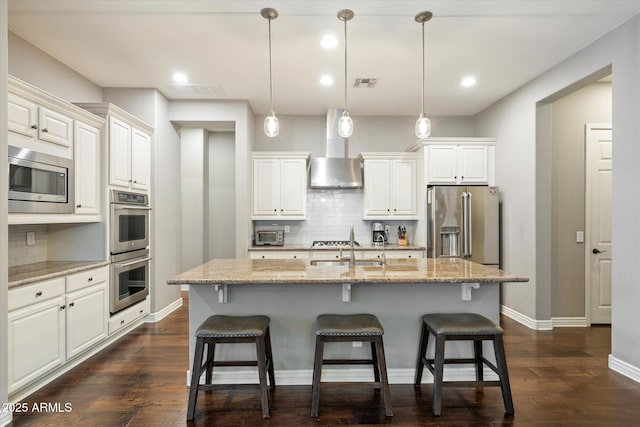 kitchen featuring visible vents, a kitchen bar, appliances with stainless steel finishes, and wall chimney exhaust hood