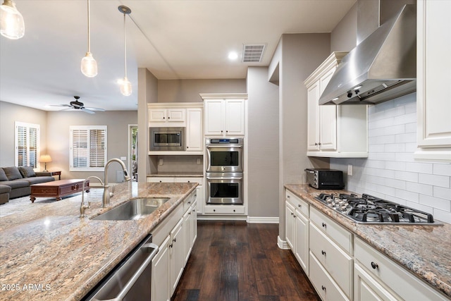 kitchen featuring visible vents, a sink, open floor plan, appliances with stainless steel finishes, and wall chimney exhaust hood