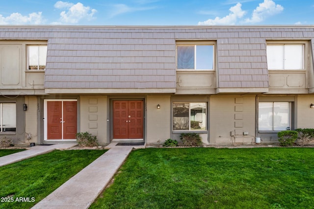 multi unit property with mansard roof, a front lawn, and brick siding