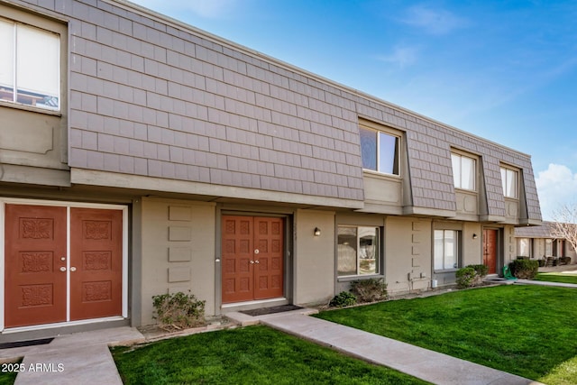 view of property featuring stucco siding, a front lawn, and mansard roof