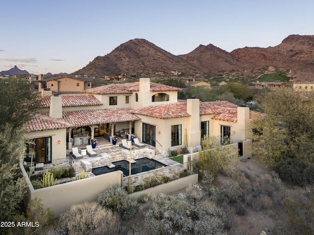 back house at dusk featuring a mountain view and a patio area