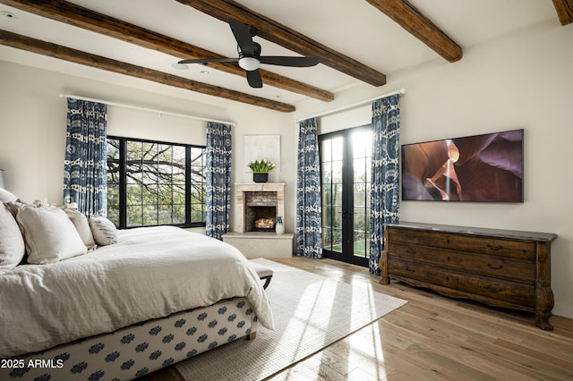 bedroom with ceiling fan, beam ceiling, multiple windows, and light hardwood / wood-style flooring