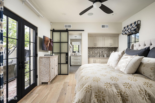 bedroom with ensuite bath, light hardwood / wood-style flooring, ceiling fan, french doors, and a barn door