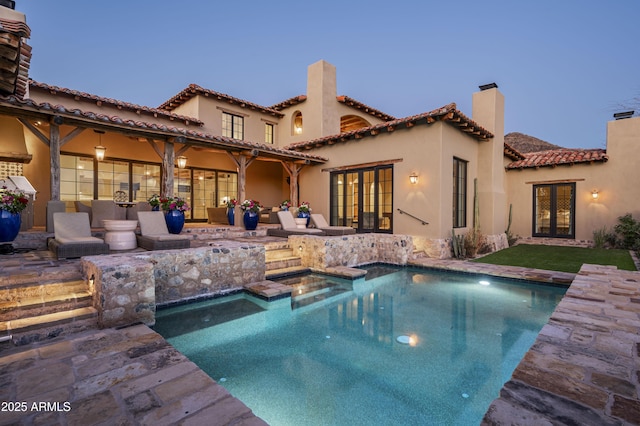 pool at dusk with french doors, a patio area, ceiling fan, and a jacuzzi