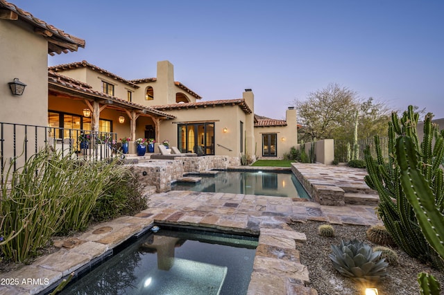 pool at dusk featuring an in ground hot tub and a patio area