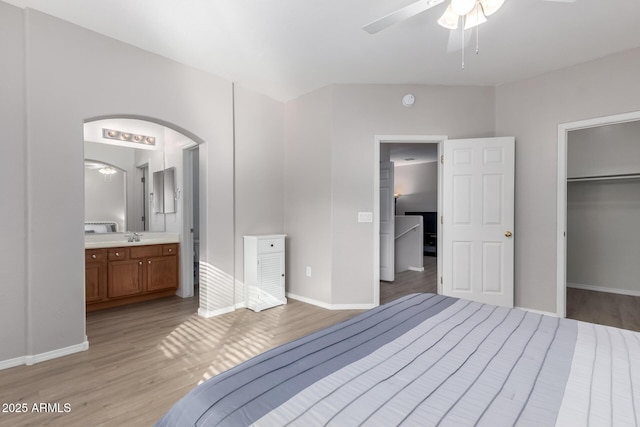 unfurnished bedroom with connected bathroom, a spacious closet, a closet, ceiling fan, and light hardwood / wood-style floors