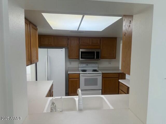 kitchen featuring a peninsula, white appliances, a sink, and brown cabinets