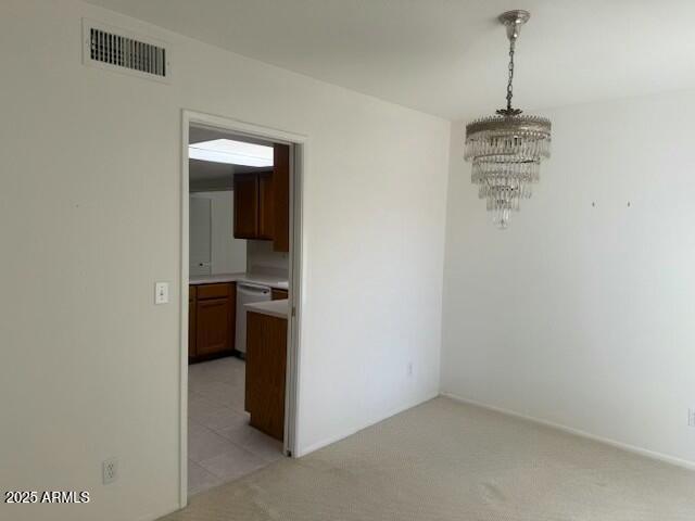 unfurnished dining area featuring light carpet, an inviting chandelier, and visible vents