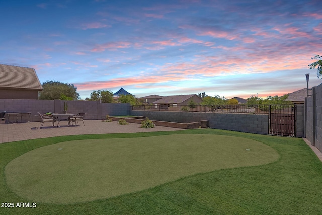yard at dusk with a putting green, a patio area, and fence