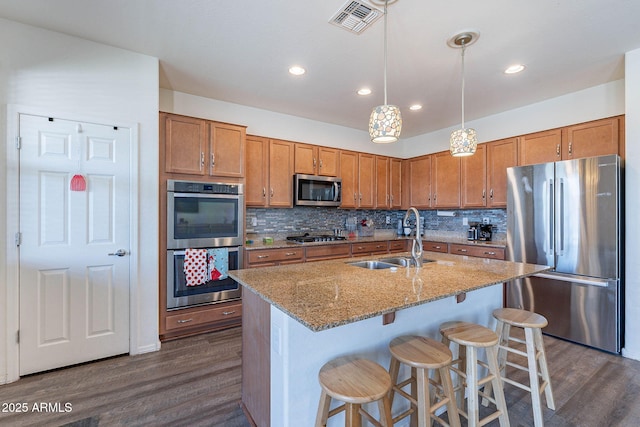 kitchen with appliances with stainless steel finishes, a sink, dark wood-style floors, brown cabinets, and recessed lighting
