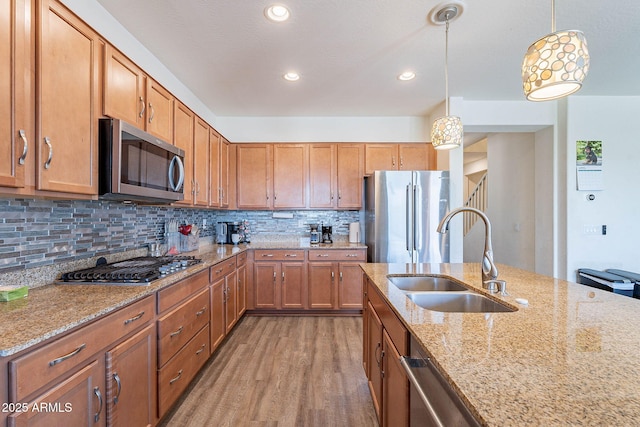 kitchen with appliances with stainless steel finishes, a sink, light wood finished floors, light stone counters, and recessed lighting